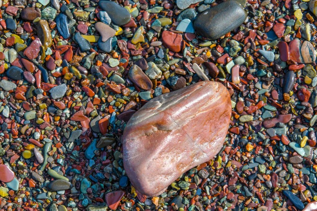 A wet, banded reddish Lake Superior agate resting among colorful polished pebbles